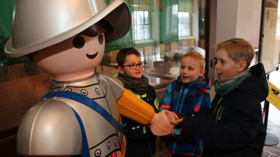 Drei Kinder vor einer riesigen Playmobil-Figur.